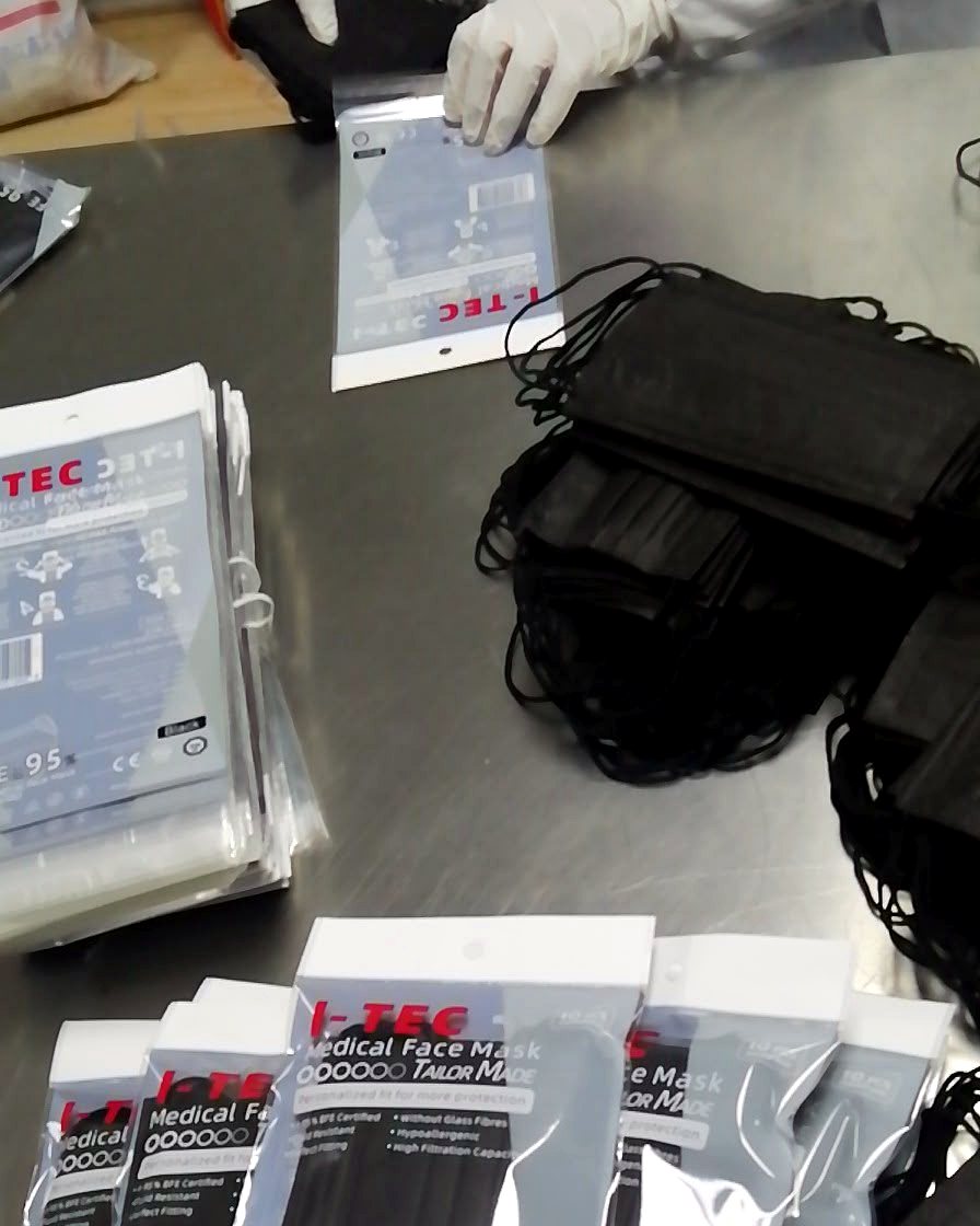 I-TEC staff in gloves packing black medical face masks into branded I-TEC retail packs at our Singapore facility